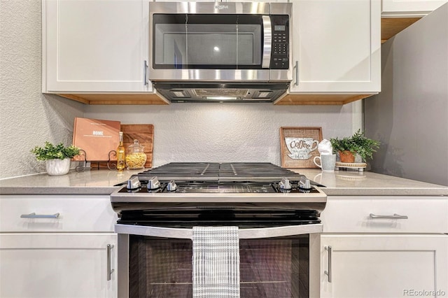 kitchen featuring white cabinets, a textured wall, stainless steel appliances, light countertops, and backsplash