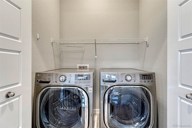 washroom featuring a textured wall, washing machine and clothes dryer, and laundry area