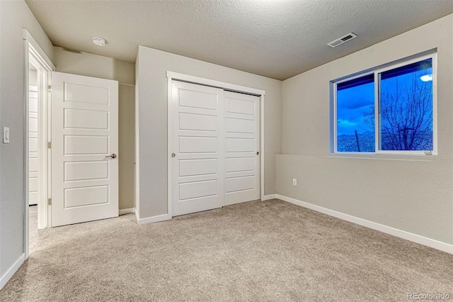 unfurnished bedroom featuring carpet floors, a closet, visible vents, a textured ceiling, and baseboards