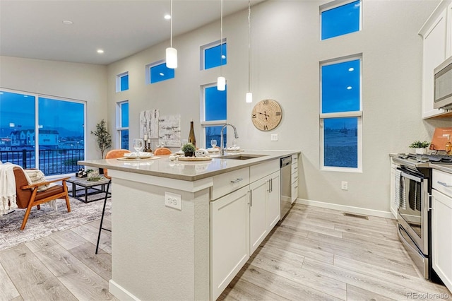 kitchen featuring a breakfast bar area, appliances with stainless steel finishes, light wood-style floors, white cabinetry, and a sink