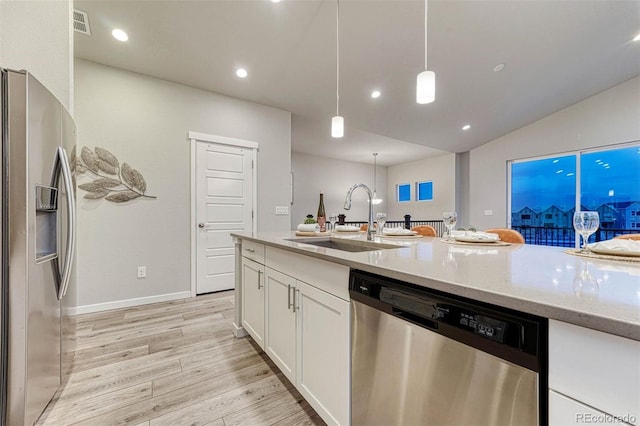 kitchen with light stone counters, stainless steel appliances, light wood-style floors, white cabinetry, and a sink