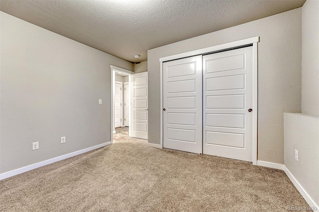 unfurnished bedroom with a closet, light colored carpet, a textured ceiling, and baseboards