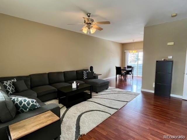 living area featuring baseboards, wood finished floors, and ceiling fan with notable chandelier