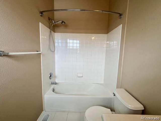 bathroom with tile patterned flooring, toilet, a textured wall, and shower / washtub combination