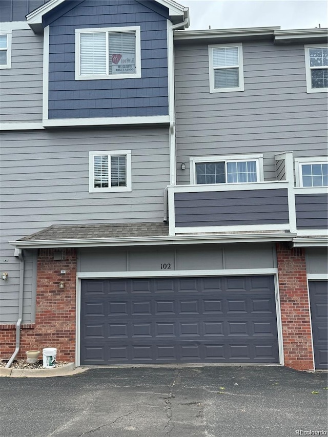 exterior space featuring a balcony, brick siding, a garage, and driveway