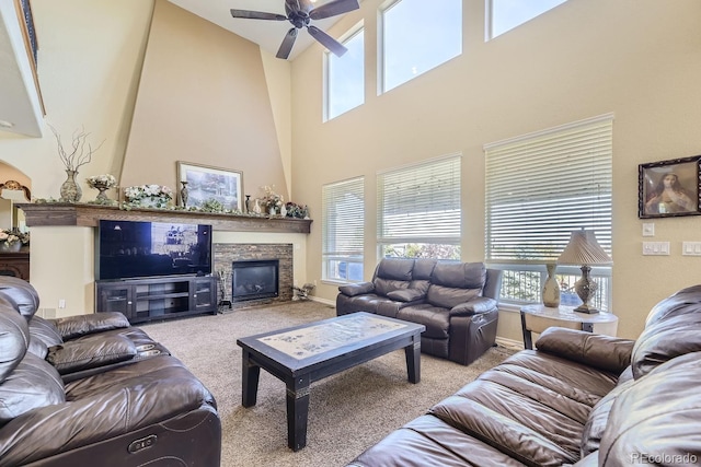 carpeted living room featuring a towering ceiling, ceiling fan, and a stone fireplace