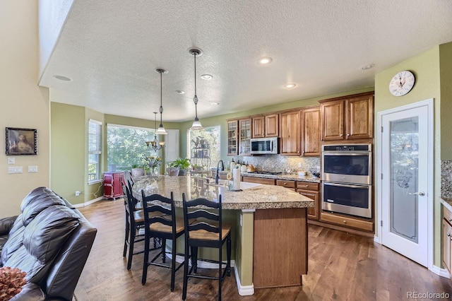 kitchen featuring a center island with sink, backsplash, stainless steel appliances, dark hardwood / wood-style floors, and a breakfast bar