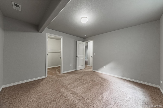 unfurnished bedroom with a closet, a spacious closet, carpet, and a textured ceiling