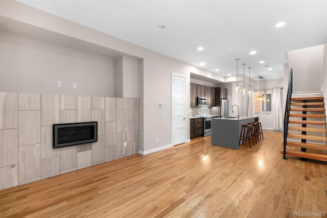 kitchen with appliances with stainless steel finishes, pendant lighting, a kitchen bar, a kitchen island with sink, and light wood-type flooring