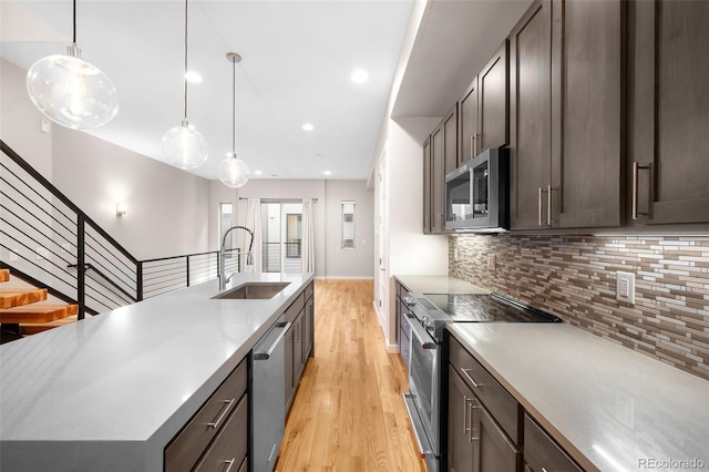 kitchen featuring appliances with stainless steel finishes, decorative light fixtures, tasteful backsplash, sink, and light hardwood / wood-style flooring