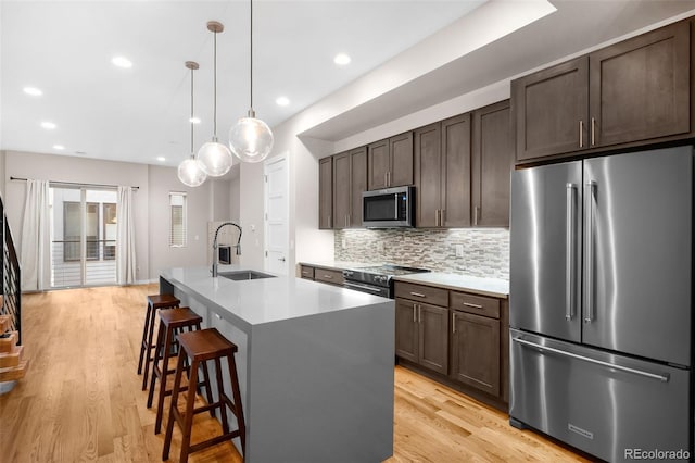 kitchen with appliances with stainless steel finishes, pendant lighting, sink, a breakfast bar area, and a kitchen island with sink