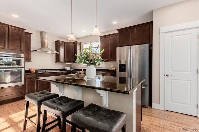 kitchen featuring a kitchen bar, appliances with stainless steel finishes, a kitchen island, decorative light fixtures, and wall chimney exhaust hood