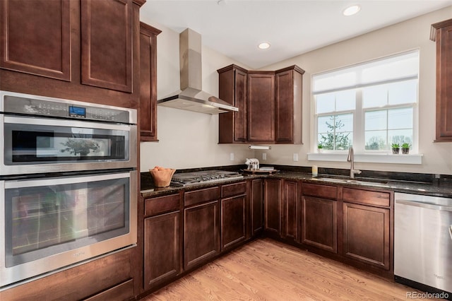 kitchen featuring sink, wall chimney exhaust hood, stainless steel appliances, and dark stone countertops