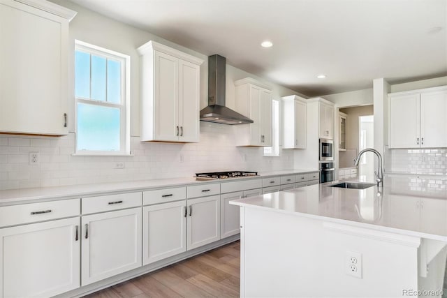 kitchen with white cabinets, a kitchen island with sink, sink, and wall chimney exhaust hood