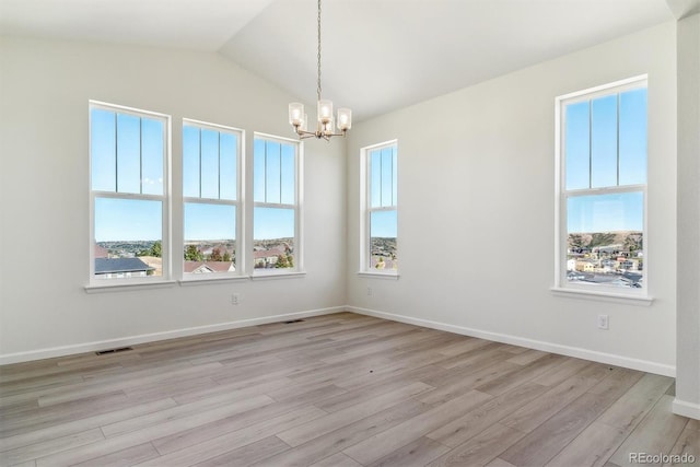 spare room featuring light hardwood / wood-style flooring, a healthy amount of sunlight, vaulted ceiling, and a notable chandelier