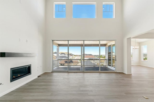 unfurnished living room featuring a towering ceiling, hardwood / wood-style flooring, and a notable chandelier