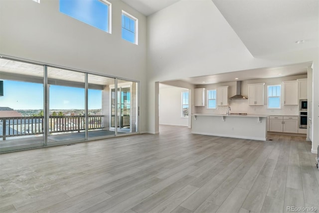 unfurnished living room featuring a towering ceiling, sink, and light hardwood / wood-style flooring