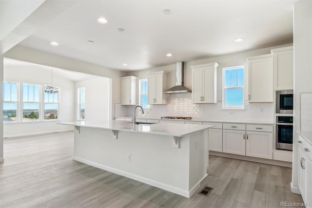 kitchen with a center island with sink, white cabinets, wall chimney range hood, sink, and stainless steel appliances