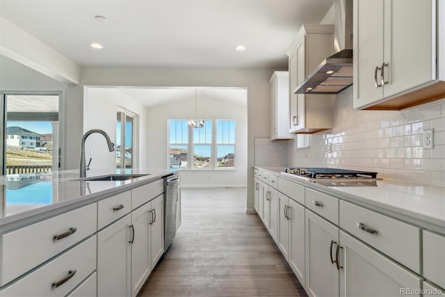 kitchen featuring sink, wall chimney range hood, lofted ceiling, decorative backsplash, and white cabinets