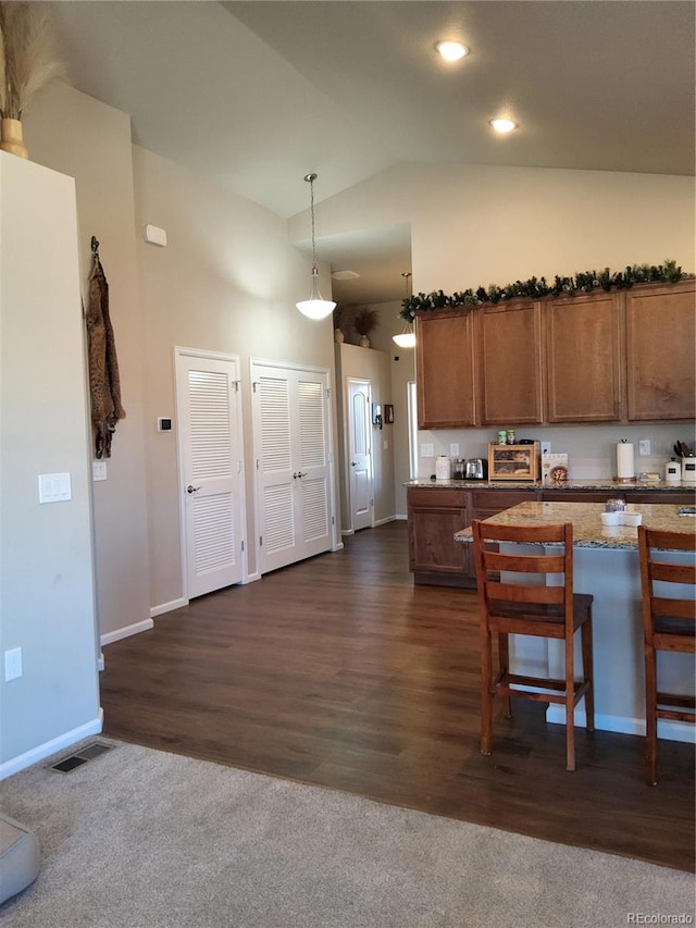 kitchen with a kitchen bar, light stone countertops, dark wood-type flooring, pendant lighting, and high vaulted ceiling