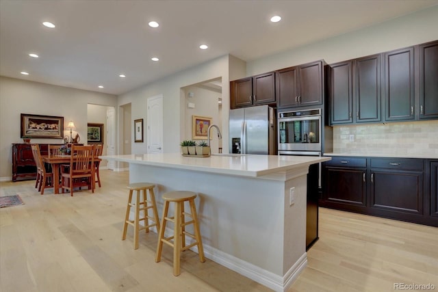 kitchen featuring stainless steel refrigerator with ice dispenser, a kitchen bar, tasteful backsplash, a center island with sink, and light wood-type flooring