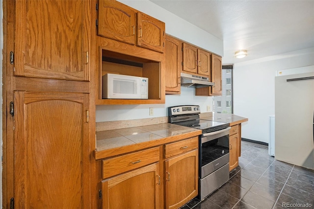 1625 Larimer St Unit 605, Denver, CO 80202 - kitchen with white appliances, under cabinet range hood, brown cabinets, tile counters, and dark tile patterned floors
