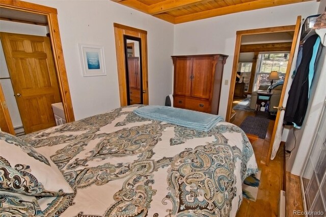 bedroom with beamed ceiling, wood ceiling, a baseboard heating unit, and hardwood / wood-style flooring