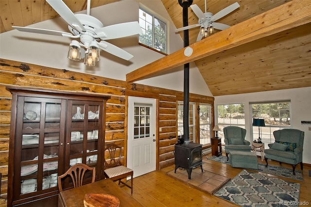 sitting room with a wood stove, rustic walls, ceiling fan, high vaulted ceiling, and hardwood / wood-style flooring