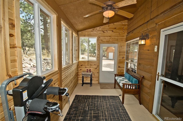 sunroom / solarium with a healthy amount of sunlight, a ceiling fan, and wood walls