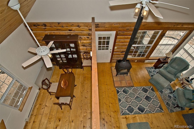 living area with baseboard heating, a wood stove, wood-type flooring, a ceiling fan, and log walls