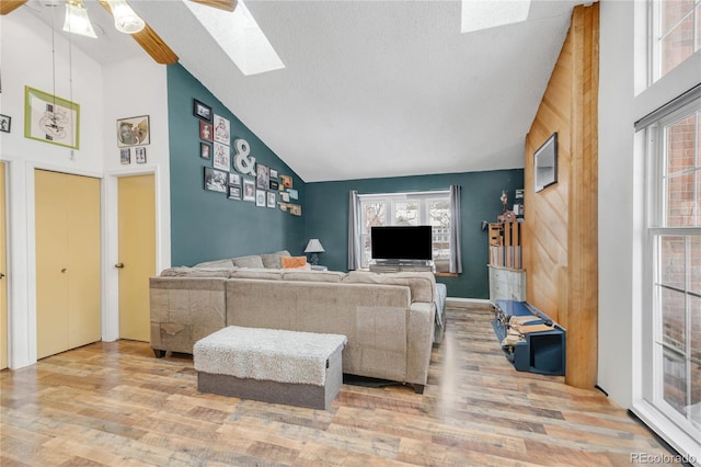 living room with light hardwood / wood-style flooring, a skylight, high vaulted ceiling, and ceiling fan