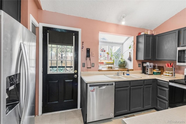 kitchen featuring lofted ceiling, sink, appliances with stainless steel finishes, a textured ceiling, and light tile patterned flooring