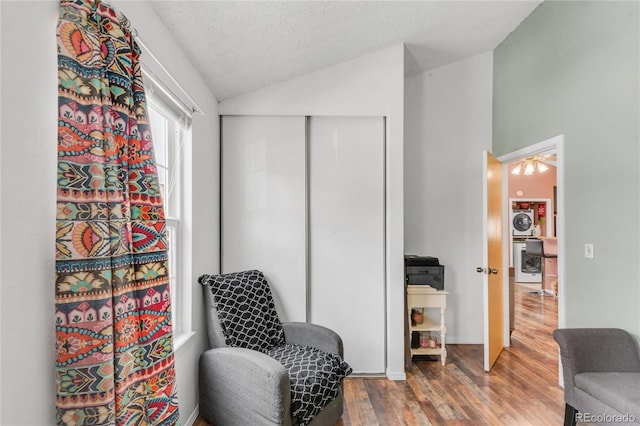 sitting room featuring wood-type flooring, washer / clothes dryer, vaulted ceiling, and a textured ceiling