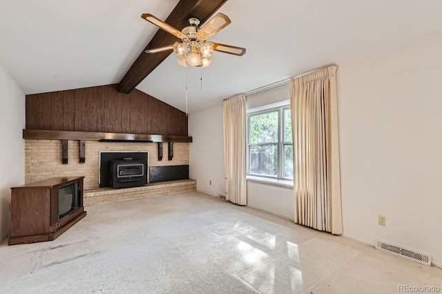 unfurnished living room featuring visible vents, a ceiling fan, a wood stove, vaulted ceiling with beams, and carpet floors