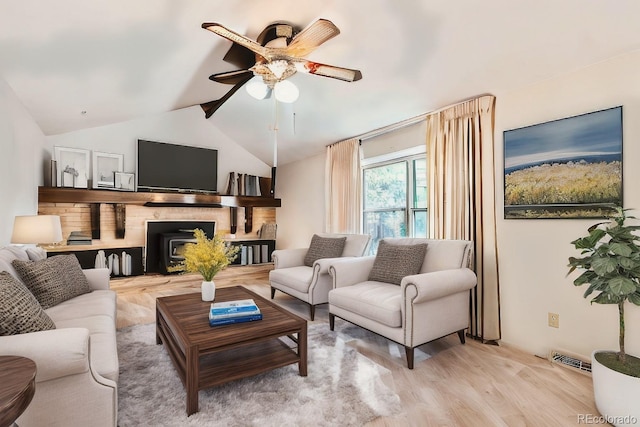 living area featuring visible vents, a ceiling fan, light wood-style flooring, a wood stove, and vaulted ceiling