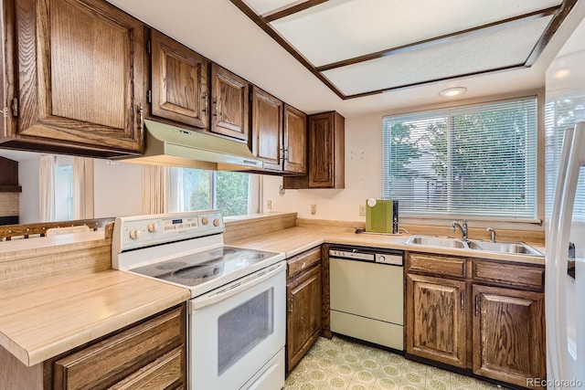 kitchen featuring under cabinet range hood, white appliances, a sink, light countertops, and light floors