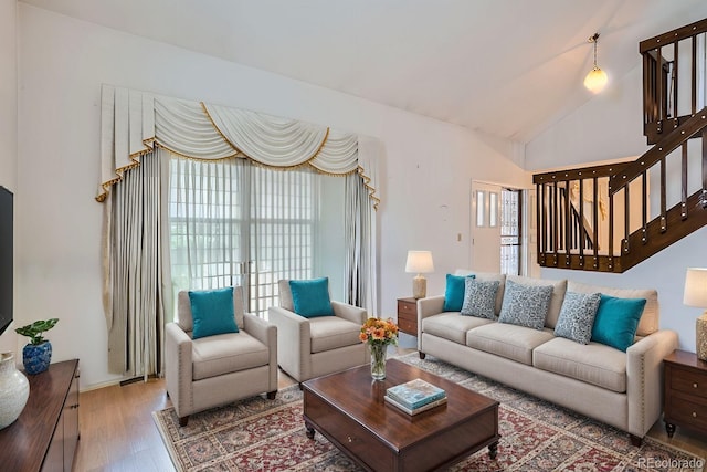 living room with stairs, vaulted ceiling, and wood finished floors