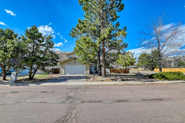 6486 Hawkeye Cir, Colorado Springs, CO 80919 - view of property hidden behind natural elements featuring an attached garage, aphalt driveway, fence, and board and batten siding