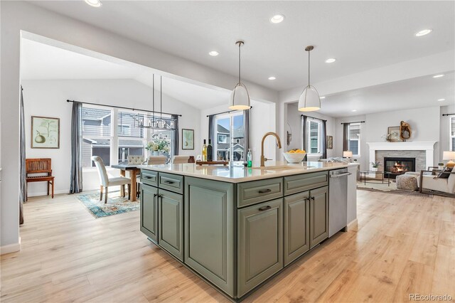 821 Boulder Peak Ave, Erie, CO 80516 - kitchen featuring a sink, light wood-style flooring, a glass covered fireplace, light countertops, and a kitchen island with sink