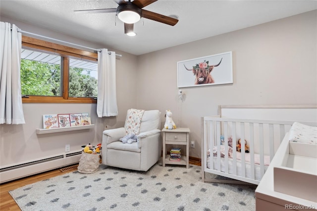2520 Eldridge Cir, Golden, CO 80401 - bedroom featuring a crib, a baseboard heating unit, wood finished floors, and a ceiling fan