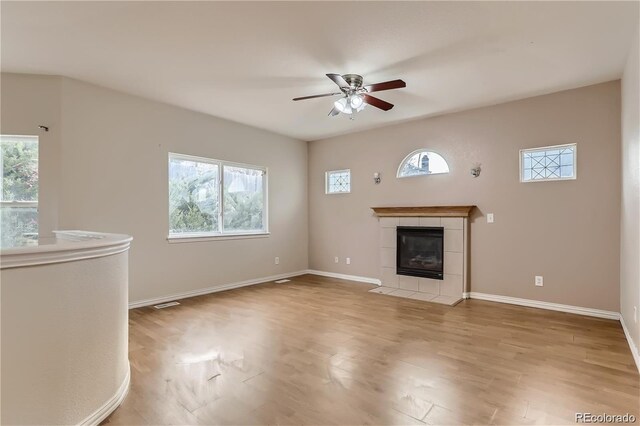 unfurnished living room featuring ceiling fan, light wood-type flooring, a tiled fireplace, and plenty of natural light