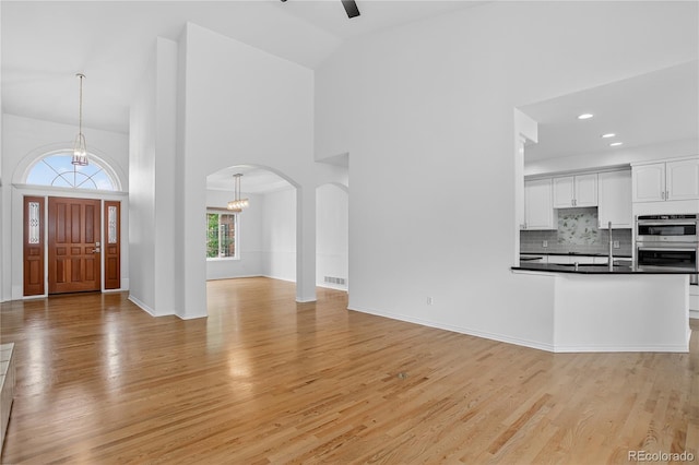 5926 S Elkhart Ct, Centennial, CO 80016 - unfurnished living room with high vaulted ceiling, a chandelier, arched walkways, light wood-style floors, and ceiling fan