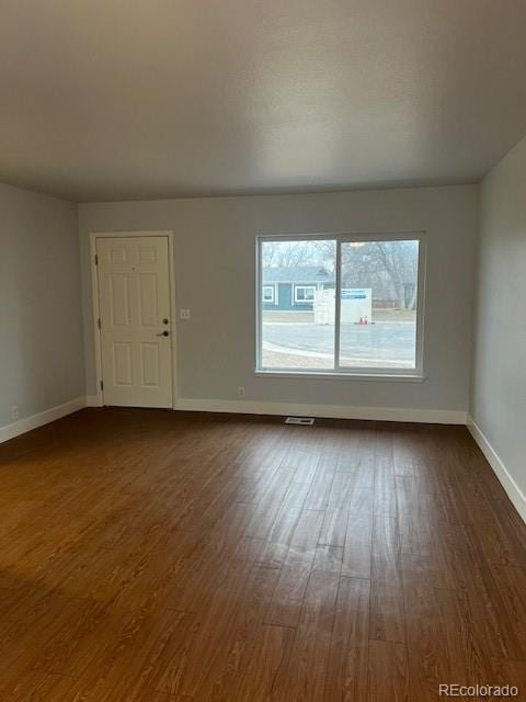 empty room featuring dark wood-style floors, visible vents, and baseboards