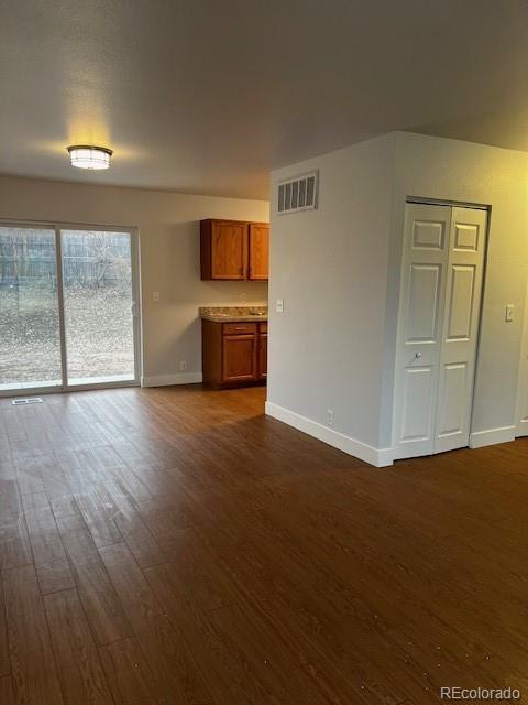 unfurnished living room with dark wood-style flooring, visible vents, and baseboards