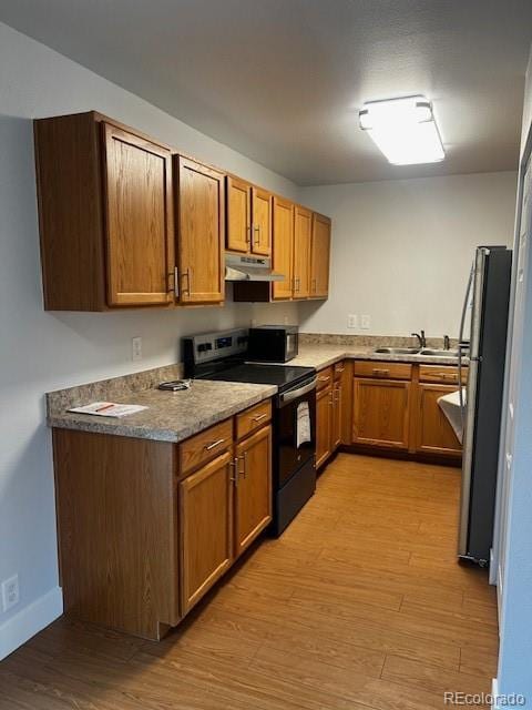 kitchen with black electric range, freestanding refrigerator, a sink, light wood-type flooring, and under cabinet range hood