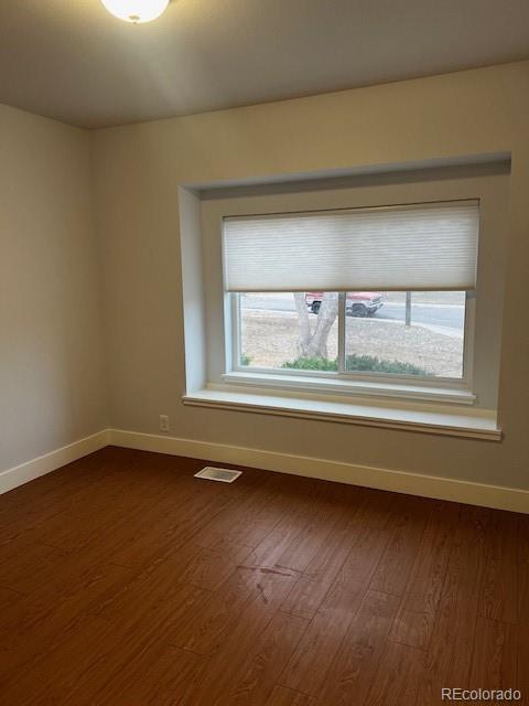 spare room with dark wood finished floors, visible vents, and baseboards