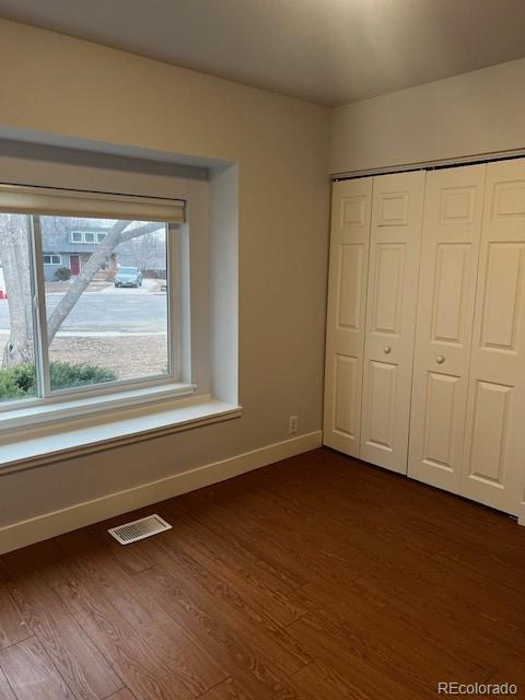 unfurnished bedroom with baseboards, a closet, visible vents, and dark wood-type flooring