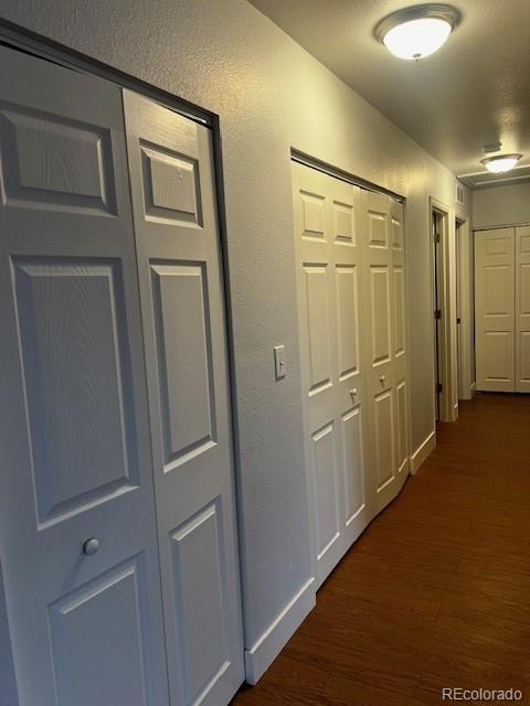 hallway with a textured wall, dark wood-style flooring, and baseboards