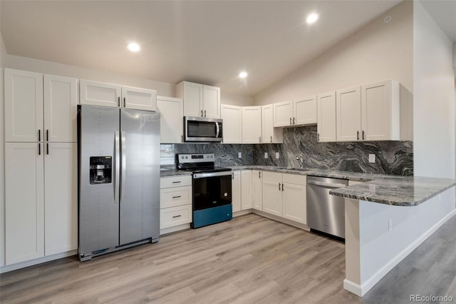 kitchen with lofted ceiling, stainless steel appliances, kitchen peninsula, and white cabinetry