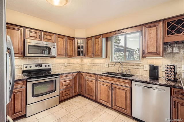 kitchen featuring dark stone countertops, backsplash, a sink, brown cabinetry, and appliances with stainless steel finishes